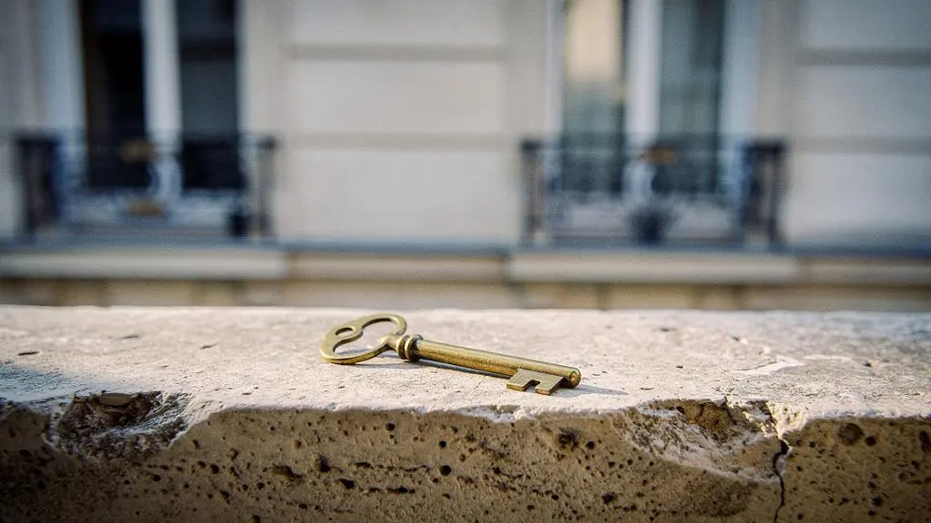 Clé en laiton posée sur le rebord en pierre d'un immeuble haussmannien parisien, symbole de l'accès à la propriété par la nue-propriété